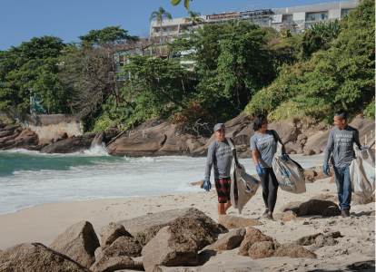 Two men and a woman walking down the beach carrying Plastic Bank bags