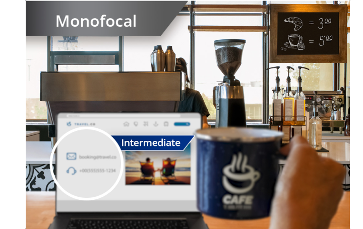 Slightly blurred image of a coffee shop with a view from the counter of coffee machines and other ingredients. A laptop is open on the countertop and an individual’s hand holds up a coffee mug to the right of the laptop screen. White text at the top left corner of this image reads “Monofocal.”
