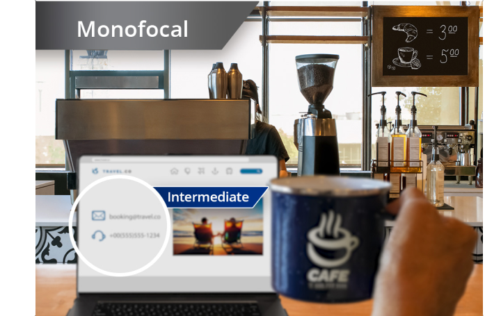 Slightly blurred image of a coffee shop with a view from the counter of coffee machines and other ingredients. A laptop is open on the countertop and an individual’s hand holds up a coffee mug to the right of the laptop screen. White text at the top left corner of this image reads “Monofocal.”