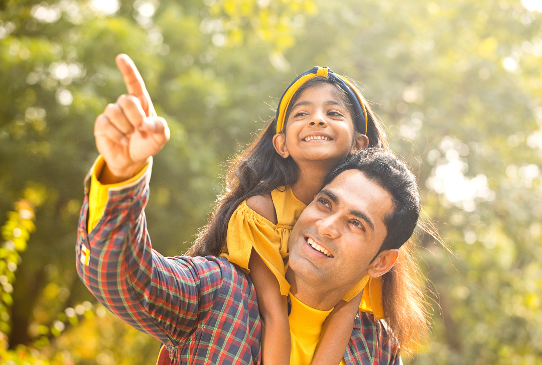 A man and a young girl looking up, both smiling, as the man is pointing at something interesting in the distance.
