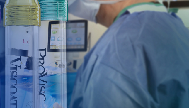 A close-up shot of three tubes of Alcon Ophthalmic Viscosurgical Devices. The tube with the purple cap is labeled DisCoVisc, the tube with the yellow cap is labelled VISCOAT, and the tube with the green cap is labelled PROVISC. Behind the tubes there is a surgeon wearing a medical mask and surgical scrubs.