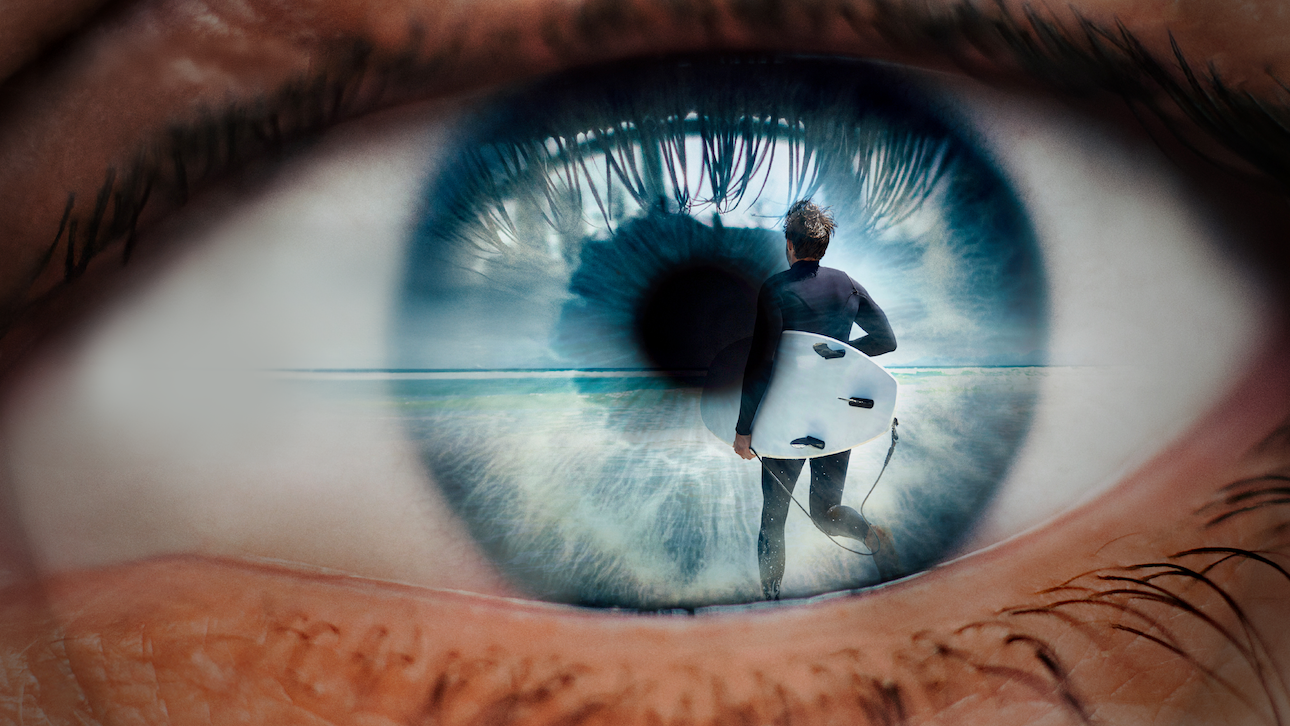 A closeup view of an eye with a surreal image imposed of a person running with a surfboard.