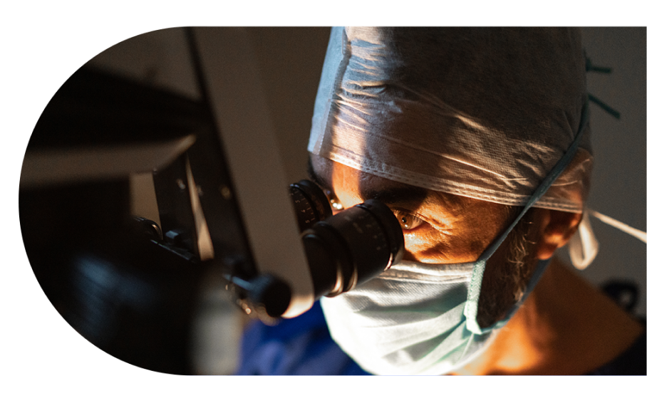 A surgeon with a mask is looking through a ophthalmic microscope. 
