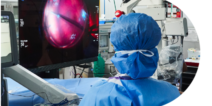 An image of a group of surgeons in an operating room with a patient undergoing surgery. An NGENUITY screen shows a close-up view of the surgery to the surgeons in the room.
