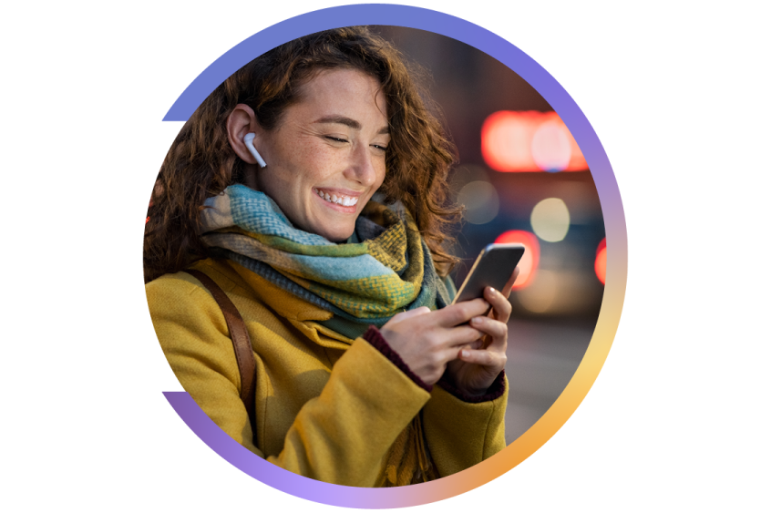 Smiling woman in a yellow coat and scarf, looking at her phone while wearing wireless earbuds