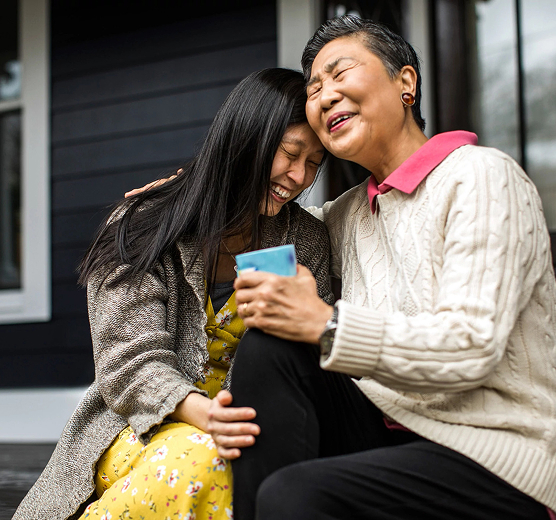 Deux femmes assises ensemble riant et partageant un moment autour d’une tasse, illustrant la connexion émotionnelle et les moments du quotidien.