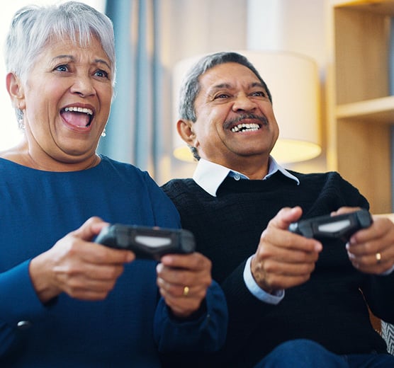 Couple âgé jouant à des jeux vidéo à la maison, souriant et engagé, illustrant un mode de vie actif et les activités visuelles du quotidien.