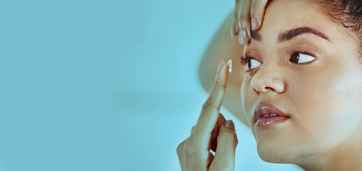 An image of an individual applying a contact lens over a blue background.