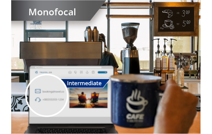 Slightly blurred image of a coffee shop with a view from the counter of coffee machines and other ingredients. A laptop is open on the countertop and an individual’s hand holds up a coffee mug to the right of the laptop screen. White text at the top left corner of this image reads “Monofocal.”