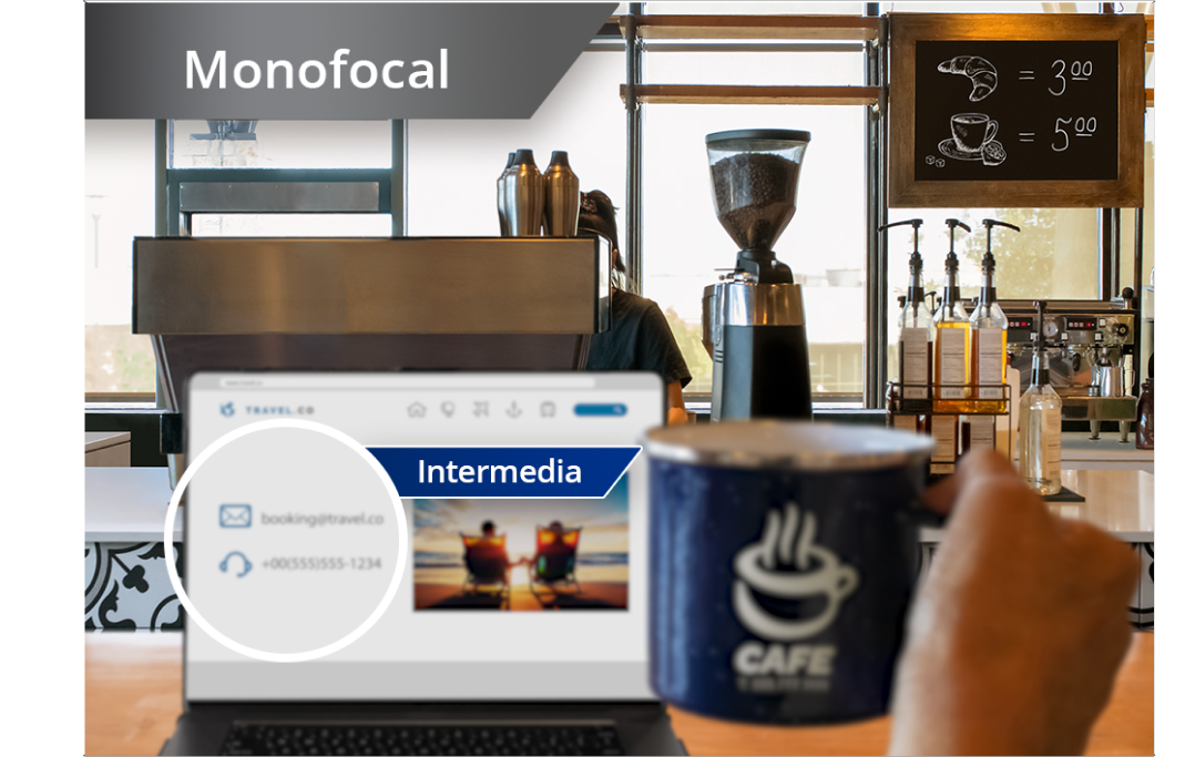 Imagen ligeramente desenfocada de cafetería con vista de la zona con cafeteras y otros ingredientes. Hay un ordenador portátil abierto sobre la barra y la mano de una persona que sujeta una taza de café a la derecha de la pantalla del portátil. Aparece un texto blanco en la esquina superior izquierda de esta imagen que dice: “Monofocal”.