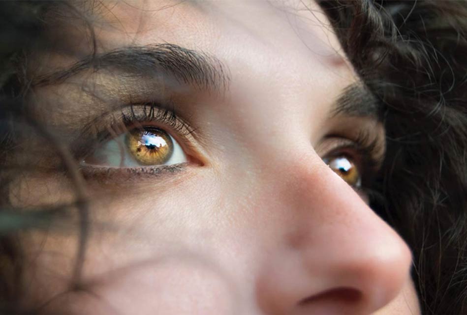 Nahaufnahme eines Frauengesichts mit strahlend haselnussbraunen Augen, die nach oben schauen, mit sanfter Beleuchtung