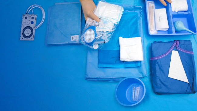 Abbildung einer Reihe von chirurgischen Materialien und Instrumente, die im Alcon Custom-Pak enthalten sein können. Die Materialien und Instrumente erscheinen auf einer blauen Fläche.