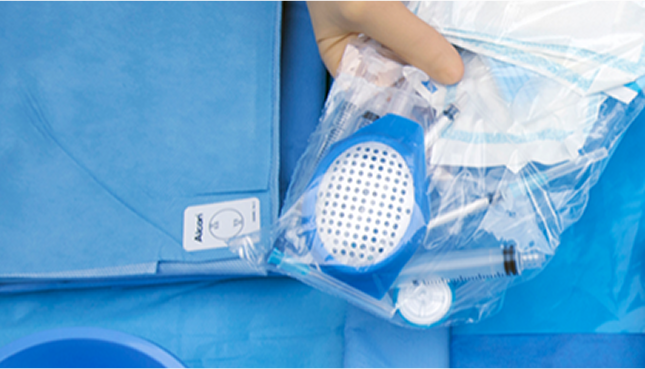 Hand, die ein steriles chirurgisches Paket mit Alcon-Instrumenten und -Materialien hält, auf einem blauen chirurgischen Tuch platziert