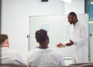 An image of a group people wearing lab coats while talking to each other, in front of a whiteboard