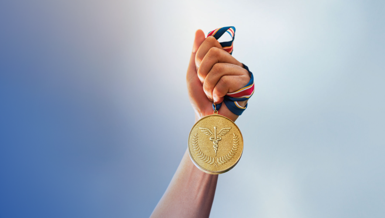 A picture of a hand holding a gold medal. Gold laurels and a caduceus appear on the medal.