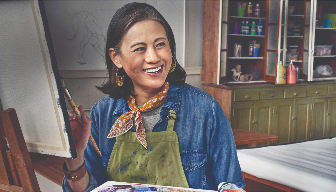 Mujer mayor que sonrie mientras sujeta un pincel ante un lienzo.