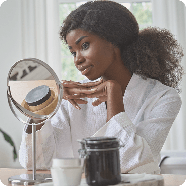 Mujer mirando su reflejo en un espejo de mesa mientras usa lentes de contacto de color FreshLook, representando un cambio sutil en la apariencia de los ojos
