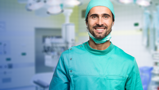 Image d'un chirurgien souriant portant une blouse chirurgicale bleu canard dans la salle d'opération.