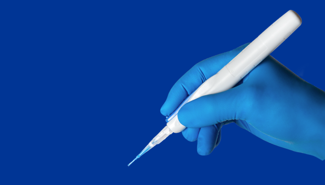 Image du système d’implantation automatisé préchargé Clareon AutonoMe tenu par une main dans un gant chirurgical bleu. La main tient le dispositif comme on tient un stylo et apparaît sur un fond bleu.
