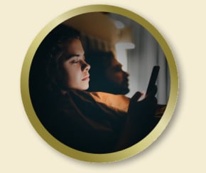 Personne regardant un smartphone dans une pièce faiblement éclairée, assise près d’une lampe allumée.