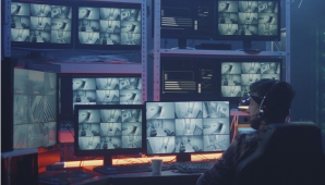 An image of a man sitting in a chair with many computer screens in front of him