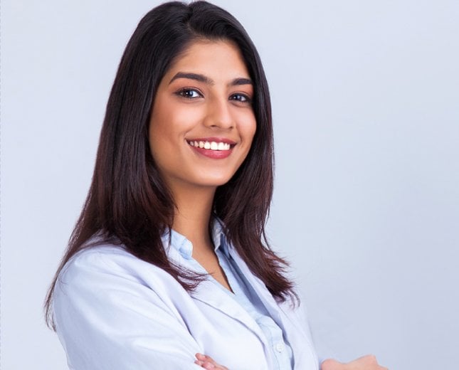 Smiling brunette woman wearing a white professional coat with arms crossed, standing against a plain light background, conveying confidence and professionalism.
