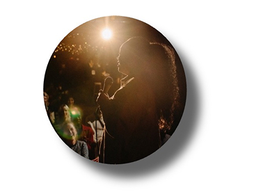 Person on stage under bright spotlight with surrounding darkness, illustrating contrast and light intensity in low-light environments