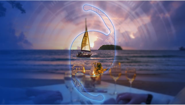 On a mostly blurred background, seen through an IOL graphic, there is a sailboat on the water during sunset, with a table set with drinks.