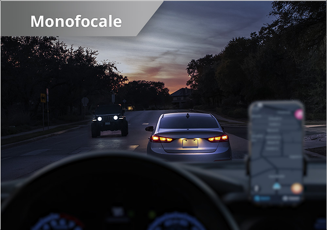 Scena simulata di guida notturna vista attraverso una IOL monofocale, con visione nitida da lontano ma schermo del navigatore dell’auto sfocato in primo piano.