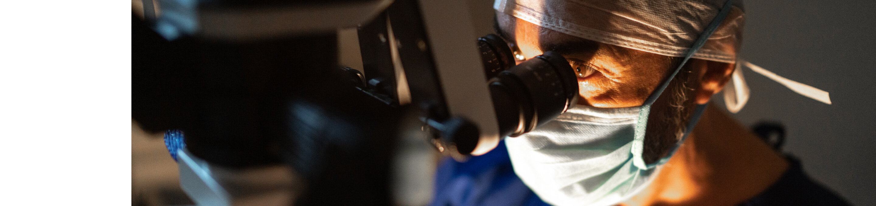 Un chirurgo con una mascherina sta guardando attraverso un microscopio oftalmico.