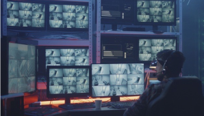 男性が椅子に座り、目の前にたくさんのコンピュータースクリーンがある画像