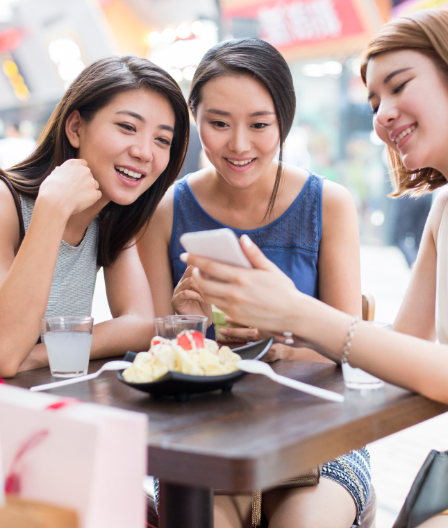 Three women sitting at a table checking something on phone