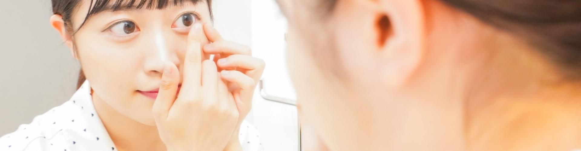Woman removing a contact lens in front of a mirror