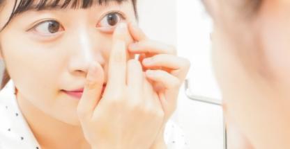 Woman removing a contact lens in front of a mirror