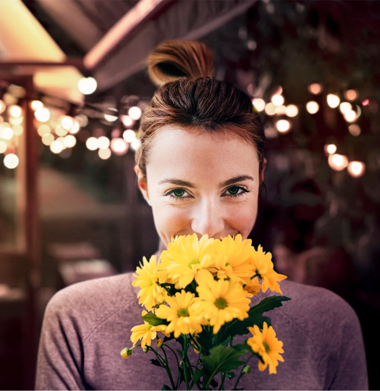 Person holding a bouquet of yellow flowers, with decorative lights blurred in the background
