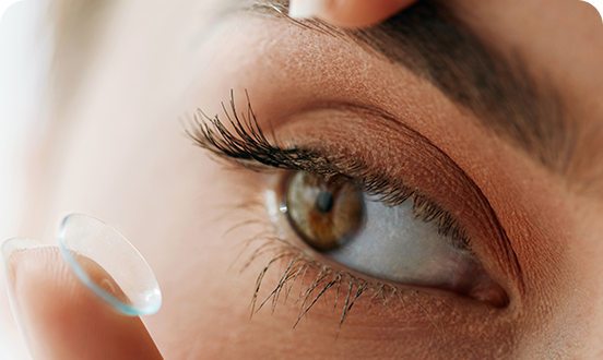Close-up of a person’s eye as they prepare to insert a contact lens, with one finger gently holding the eyelid open and the contact lens resting on their fingertip
