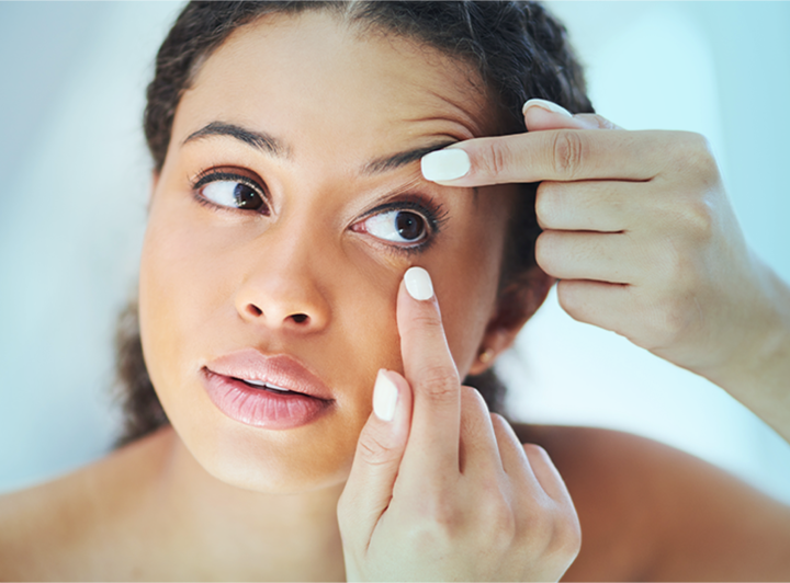 Woman looking into mirror and inserting monthly contact lenses