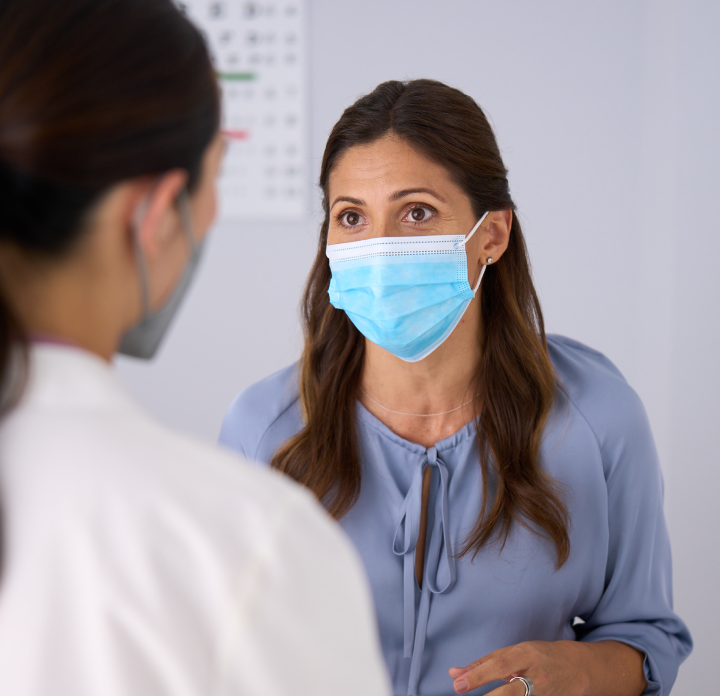 Woman having conversation with her doctor, both wearing masks
