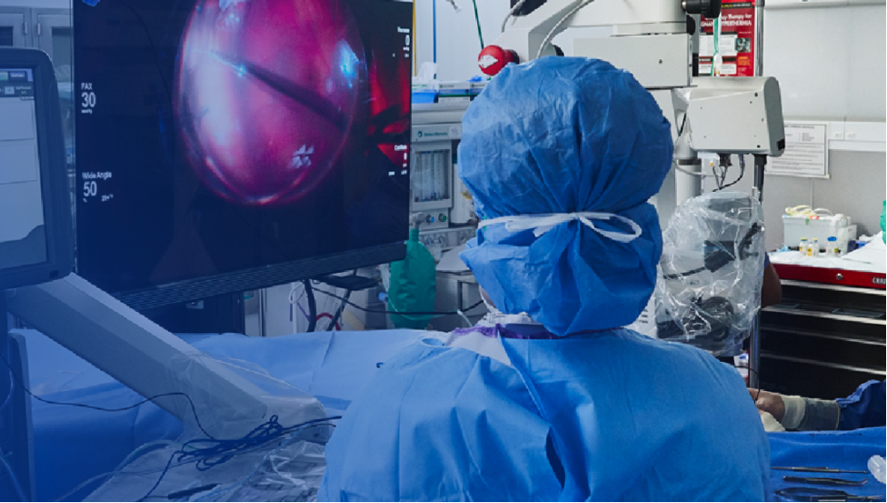 An image of a group of surgeons in an operating room with a patient undergoing surgery. An NGENUITY screen shows a close-up view of the surgery to the surgeons in the room.