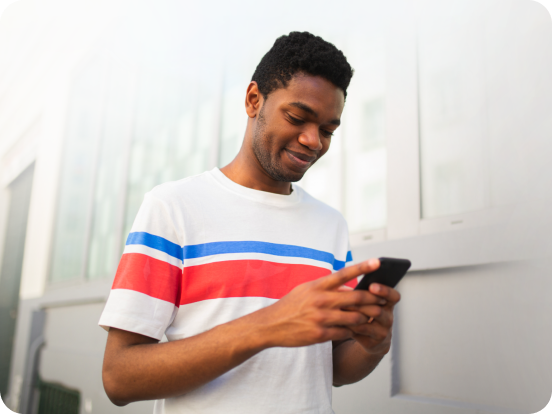 man with red and blue striped tshirt looking at phone while smiling