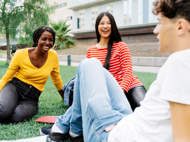 Group of students sitting on the grass outdoors, laughing and talking together on campus