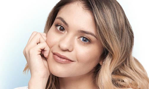 Portrait of a young woman with light brown hair, resting her face on her hand and wearing a blue color contact lens in one eye