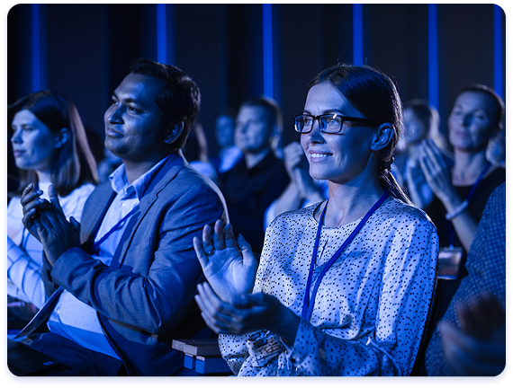 A group of conference attendees sitting in a conference room during a presentation and clapping