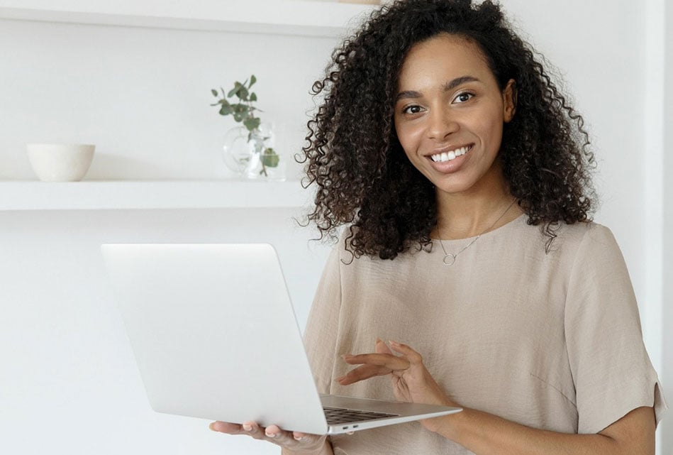 Smiling woman standing indoors in front of an open laptop