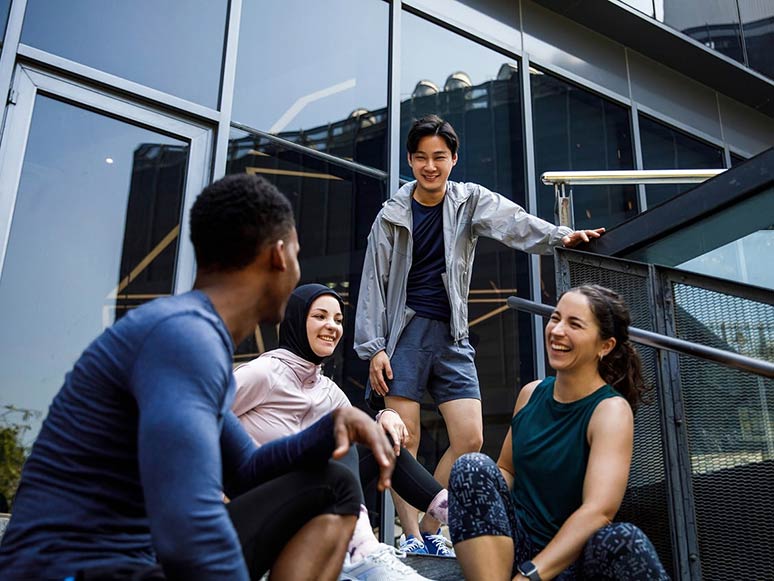 Friends gathered on outdoor steps near a modern building, smiling and chatting after exercising