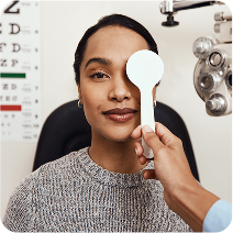A woman undergoes an eye exam with an occluder held by a professional.
