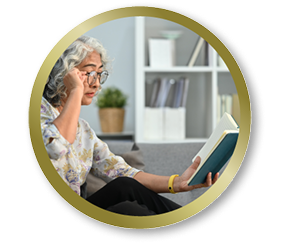 Older woman sitting on a couch reading a book while adjusting her glasses