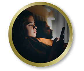 Woman in bed using her phone in low light, representing everyday visual comfort needs