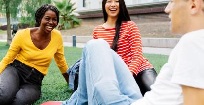 Group of students sitting on the grass outdoors, laughing and talking together on campus