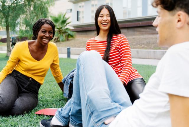 Group of students sitting on the grass outdoors, laughing and talking together on campus